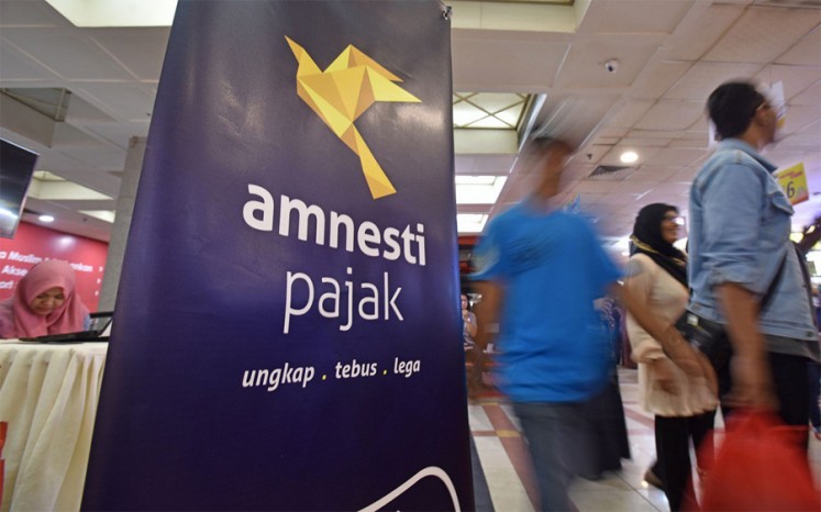 Mencari pendapatan negara: Orang-orang melewati spanduk yang mempromosikan amnesti pajak pemerintah di pasar tekstil Tanah Abang, Jakarta, di tahun 2016.